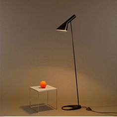 an orange sitting on top of a white table next to a black floor lamp with a cord