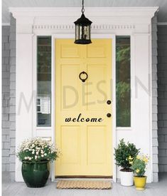 a yellow door with the words welcome on it and two potted plants next to it