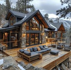 a large wooden deck with couches on it in front of a mountain cabin style home