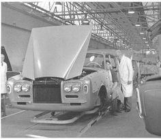 an older man standing next to a car with its hood open in a garage area