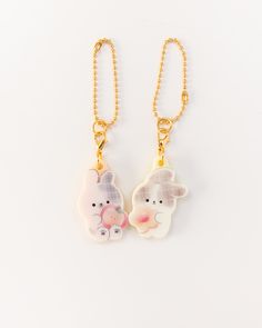 two keychains with animals on them hanging from gold chain necklaces against a white background