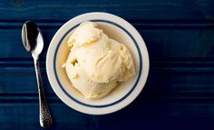 two scoops of ice cream sit in a bowl next to a spoon on a blue table