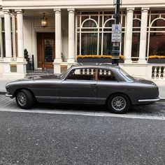 an old car parked on the side of the road in front of a large building