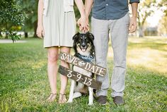 a man and woman standing next to a dog in front of a sign that says save the date