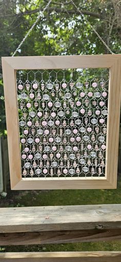 a wooden frame hanging from the side of a tree with pink flowers on it in front of a fence