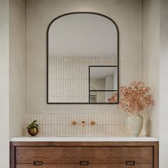 a bathroom with a large mirror above the sink and wooden drawers below it, along with a vase filled with flowers