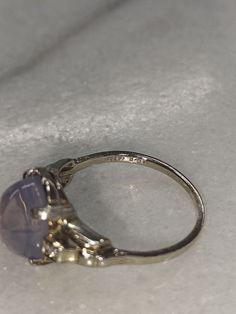 a silver ring with a purple stone on it sitting on a white tablecloth covered surface