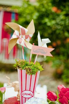 an arrangement of flowers in a red and white striped vase with paper windmills on top