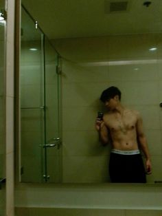 a shirtless man taking a selfie in the bathroom mirror with his cell phone