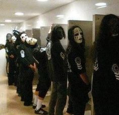 a group of people wearing masks standing next to each other in a hallway with urinals