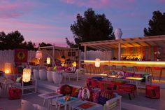 an outdoor seating area is lit up at night with colorful lights on the tables and chairs