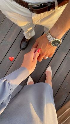 two people holding hands while sitting on a wooden floor with hearts in the air above them