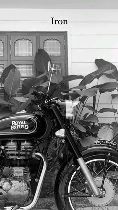 a black and white photo of a royal enfield motorcycle parked in front of a house