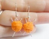 a pair of orange yarn wrapped in silver earwires on a person's hand