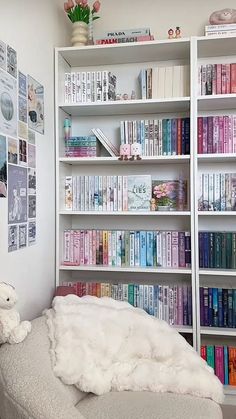 a white bookcase filled with lots of books next to a teddy bear sitting on a chair