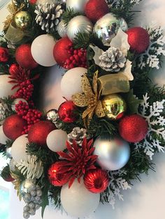 a christmas wreath with red and white balls, pine cones, silver ornaments and evergreen leaves