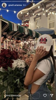 a woman wearing a hat standing in front of flowers