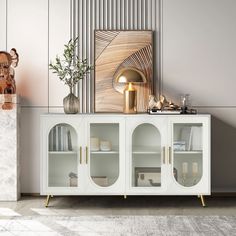 a white cabinet with glass doors and gold handles next to a vase on a table