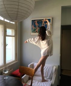 a woman standing on top of a bed next to a window