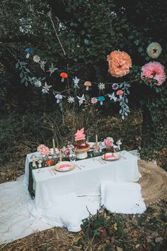 a table set up with flowers and candles for a wedding reception in the woods on a blanket