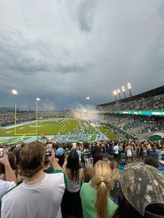 a stadium filled with lots of people standing on top of a field under cloudy skies