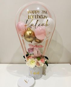 a vase filled with balloons and flowers on top of a white table next to a card