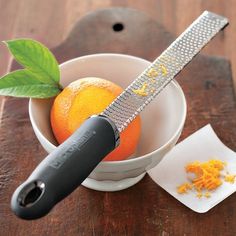 an orange is in a bowl with a knife on the table next to it's peeler