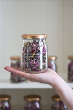 a person holding up a jar filled with flowers in front of other jars on shelves