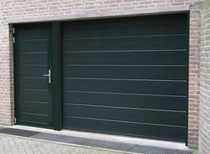 a green garage door with brick wall and cobblestone sidewalk in front of it