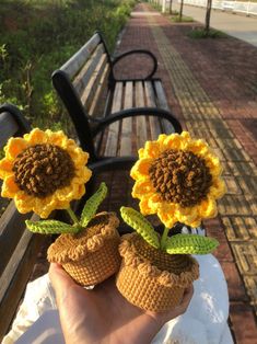 two crocheted sunflowers sitting on top of each other in front of a bench