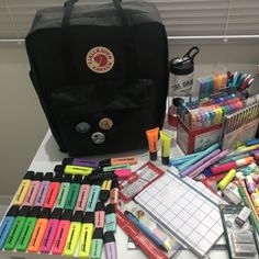 an assortment of pens, markers and other items on a table with a black bag