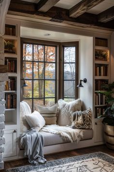 a window seat with pillows and blankets on it in front of a book shelf filled with books