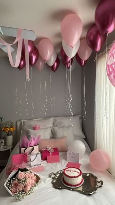 a bed with pink and white balloons hanging from it's ceiling, next to a cake on a tray