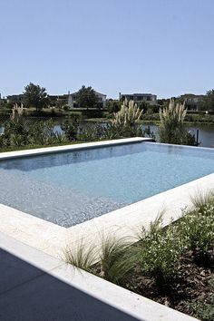 an empty swimming pool in the middle of a field with trees and bushes around it