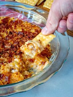 a person dipping a piece of pizza into a casserole dish with cheese and meat