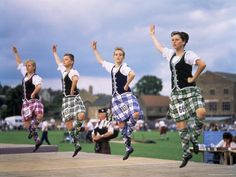 a group of men and women in kilts jumping on a stage at a highland festival