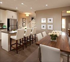 a dining room table with white chairs and pictures on the wall in front of it