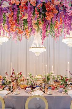 a table with flowers hanging from the ceiling and chandelier above it, surrounded by candles