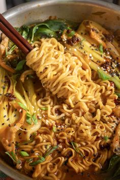 a bowl filled with noodles and vegetables next to chopsticks on top of a table