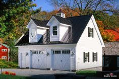 a white house with black shingles and two garages on the side of it