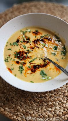 a white bowl filled with soup sitting on top of a woven place mat next to a wooden table