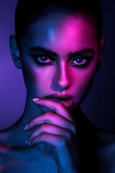 a woman with dark makeup and purple light on her face, posing for the camera