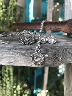 three pieces of jewelry sitting on top of a piece of wooden plank next to a tree branch