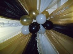 black, white and gold balloons are hanging from the ceiling