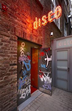 two doors with graffiti on them in front of a red brick building that says disco