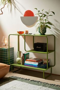 a green shelf with books, plants and other items on it next to a white wall