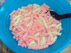 a blue bowl filled with pasta on top of a wooden table next to a black spatula