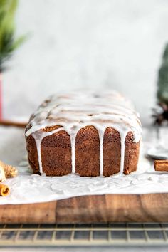 a loaf of bread with icing sitting on top of a wooden cutting board next to cinnamon sticks