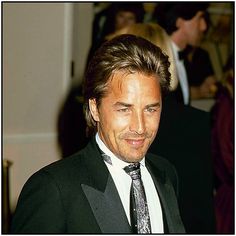 a man wearing a suit and tie in a room with other people looking at the camera