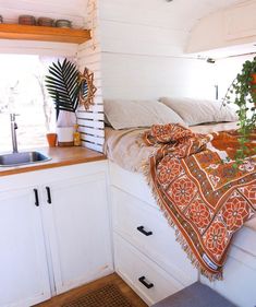 a bed in a small room next to a sink and window with plants on it